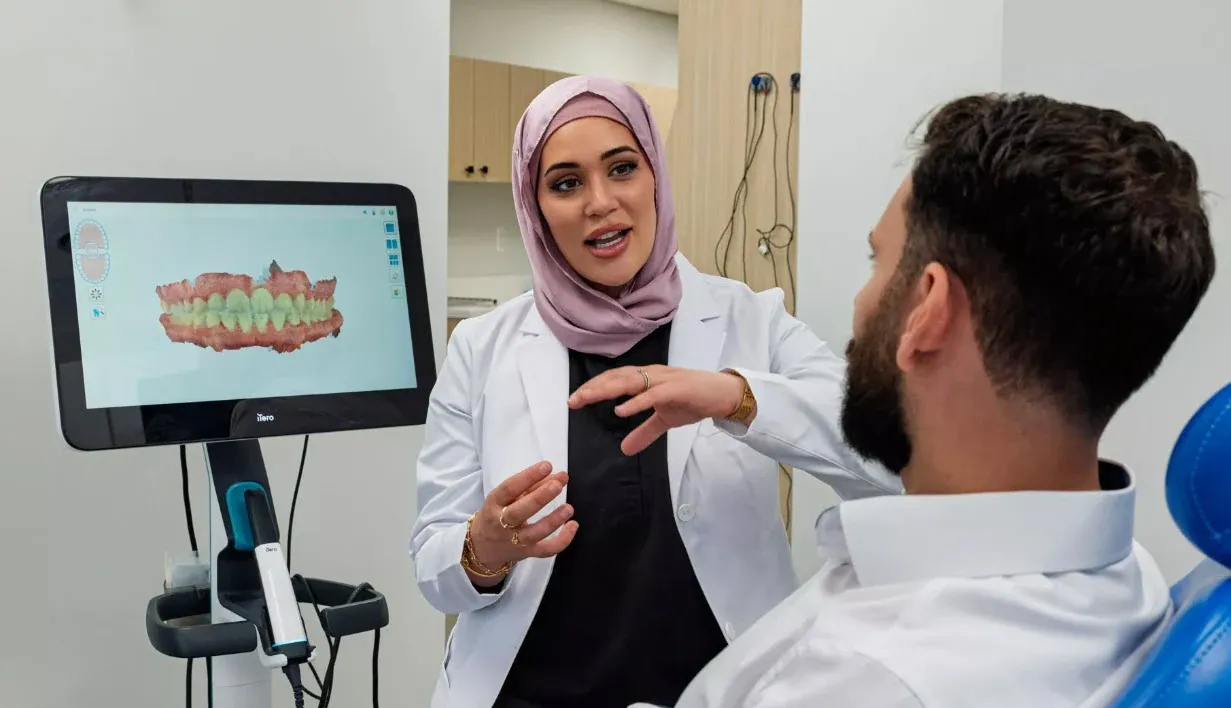A dental clinician and a smiling patient discussing treatment together in the operatory