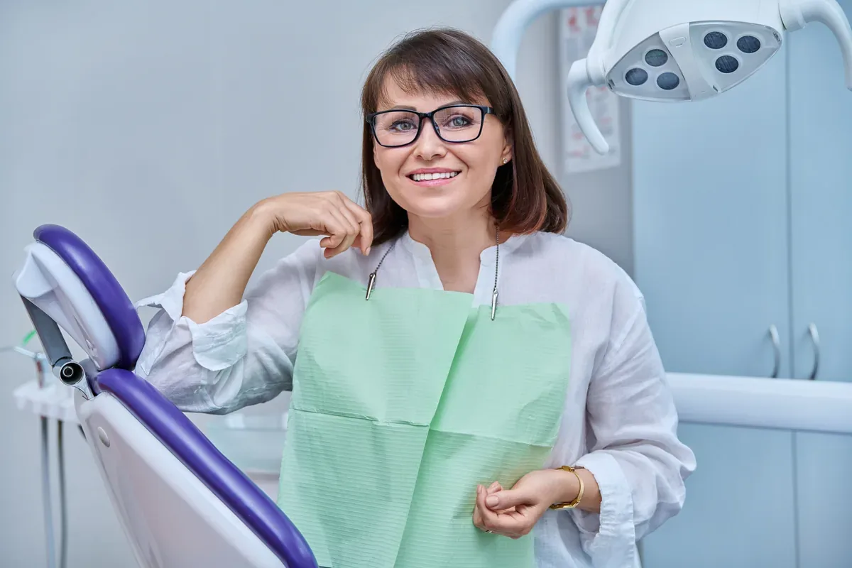 A smiling woman in her forties seated in the dental chair — Dental Bridges at SmilePro Dental
